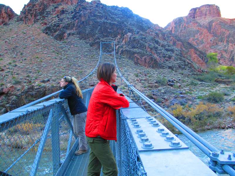 two women on a suspension bridge overlooking a river in a Grand Canyon valley